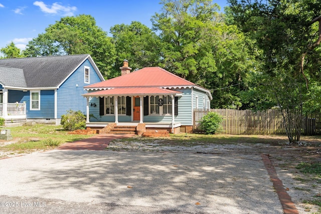 312 E W St, Southport, NC 28461 - view of front of house with a porch, fence, a chimney, and metal roof
