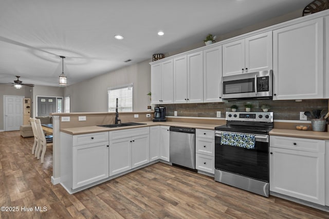 kitchen with stainless steel appliances, a sink, a peninsula, white cabinets, and recessed lighting