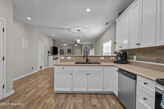 kitchen featuring stainless steel dishwasher, a sink, a peninsula, white cabinets, and tasteful backsplash
