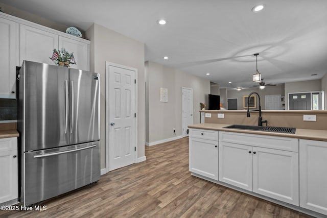 kitchen with freestanding refrigerator, a sink, ceiling fan, white cabinets, and wood finished floors