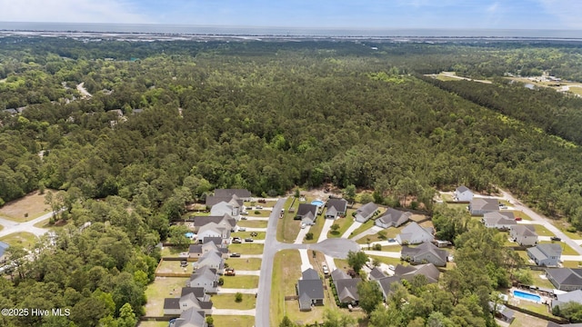 aerial view of property and surrounding area featuring a forest and nearby suburban area