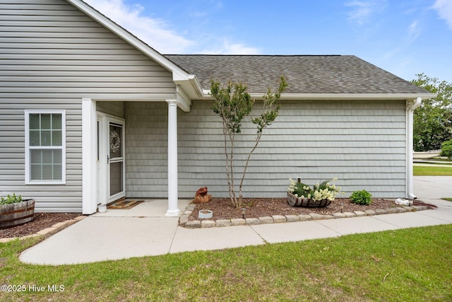 entrance to property featuring a shingled roof and a patio area