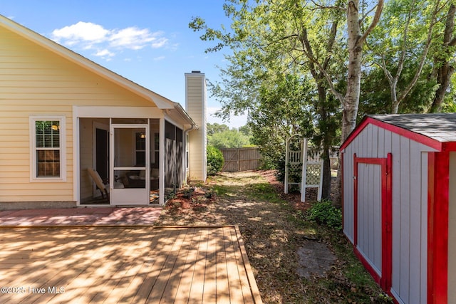 deck featuring fence, an outdoor structure, a sunroom, and a storage shed