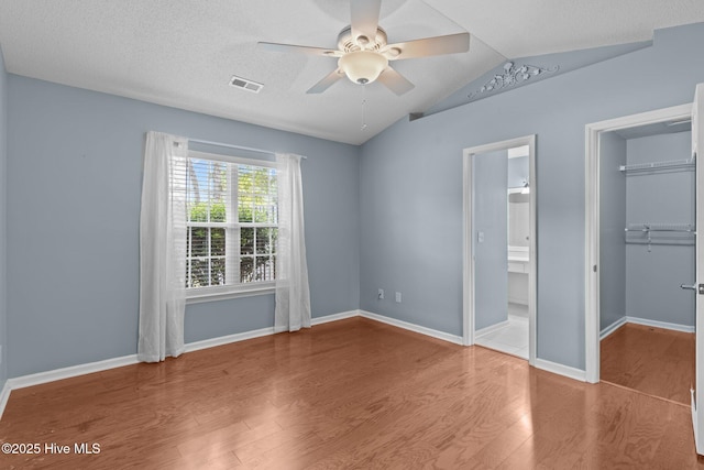 unfurnished bedroom with visible vents, a walk in closet, wood finished floors, and vaulted ceiling