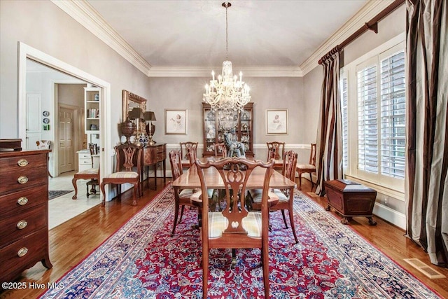 dining room with crown molding, an inviting chandelier, wood finished floors, and visible vents