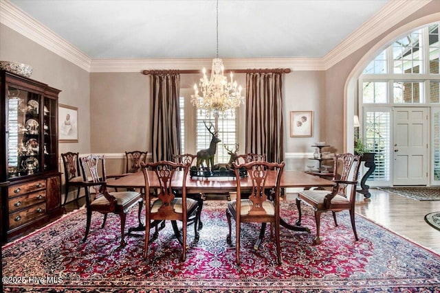 dining space featuring arched walkways, an inviting chandelier, ornamental molding, and wood finished floors