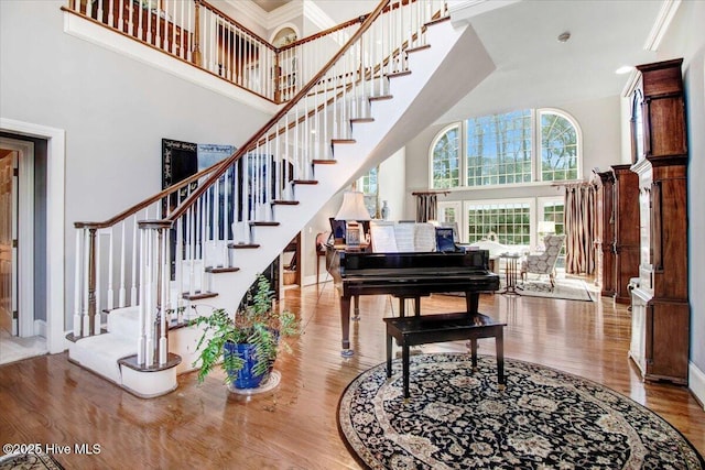 interior space with a towering ceiling, wood finished floors, stairway, baseboards, and ornamental molding