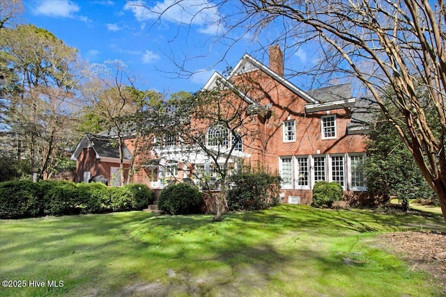 tudor house with a chimney, a front lawn, and brick siding