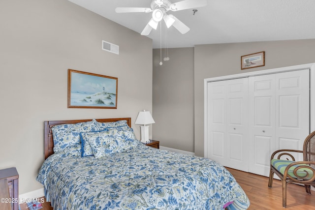 bedroom featuring ceiling fan, visible vents, wood finished floors, baseboards, and a closet