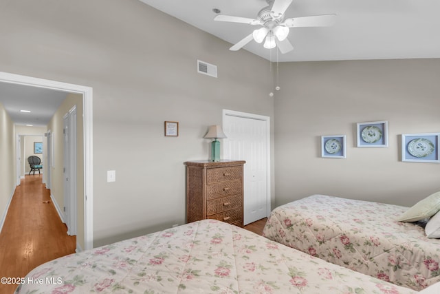 bedroom featuring ceiling fan, visible vents, wood finished floors, a closet, and a high ceiling