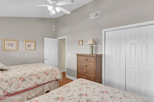 bedroom with visible vents, a closet, wood finished floors, baseboards, and high vaulted ceiling