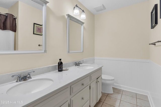 bathroom with double vanity, a sink, a wainscoted wall, and toilet