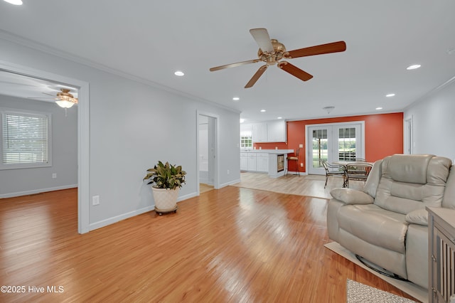 living area with crown molding, a ceiling fan, and light wood finished floors