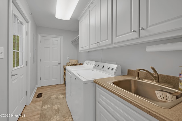 laundry room featuring visible vents, cabinet space, a sink, light wood finished floors, and washer and dryer