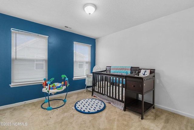 carpeted bedroom with baseboards, a nursery area, and visible vents