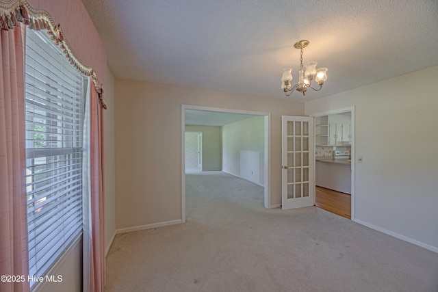 carpeted empty room with french doors, baseboards, and an inviting chandelier