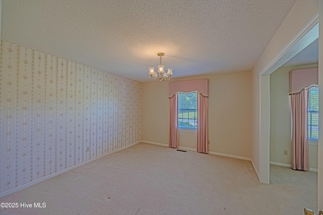 empty room with visible vents, carpet flooring, a textured ceiling, and a notable chandelier