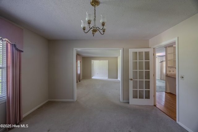 carpeted spare room featuring an inviting chandelier, baseboards, and a textured ceiling