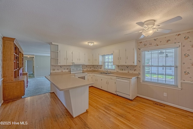 kitchen featuring white appliances, a peninsula, a sink, and light wood-type flooring