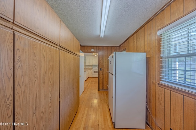 kitchen with brown cabinetry, freestanding refrigerator, wooden walls, a textured ceiling, and light wood finished floors