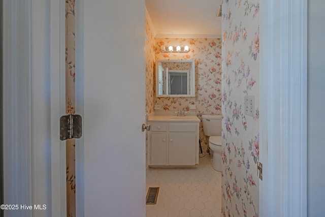 bathroom featuring vanity, toilet, wallpapered walls, visible vents, and ornamental molding
