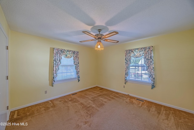 carpeted spare room featuring plenty of natural light, a ceiling fan, and visible vents