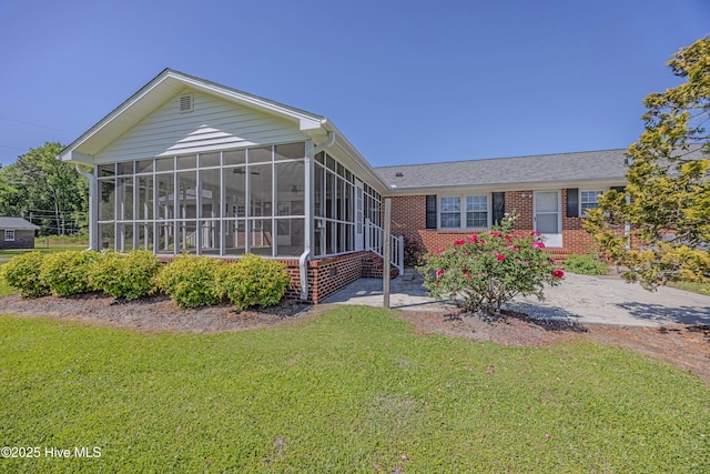 back of property with a yard, a sunroom, and brick siding