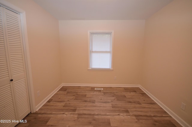 unfurnished bedroom featuring a closet, baseboards, wood finished floors, and visible vents