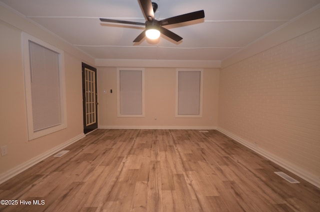 unfurnished room featuring visible vents, a ceiling fan, light wood-style flooring, and brick wall