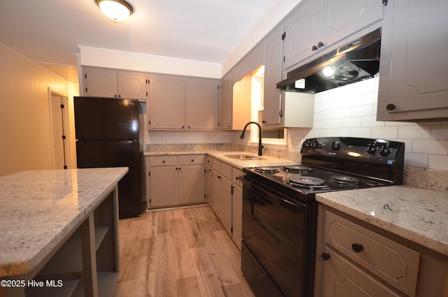 kitchen featuring light wood-style floors, under cabinet range hood, a sink, backsplash, and black appliances