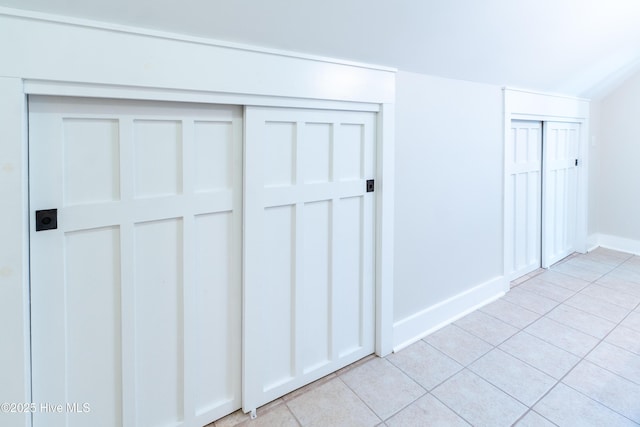 unfurnished bedroom with light tile patterned floors, baseboards, and multiple closets
