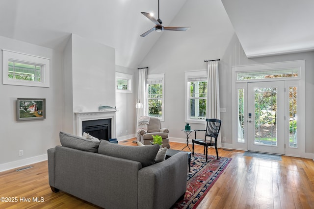 living room featuring a fireplace, high vaulted ceiling, light wood-type flooring, ceiling fan, and baseboards