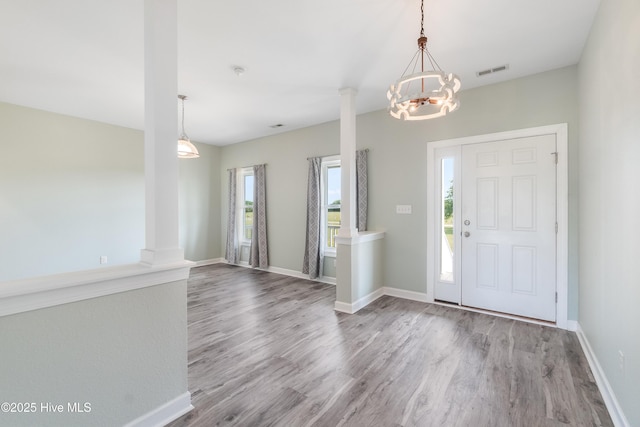 foyer entrance with visible vents, wood finished floors, baseboards, a notable chandelier, and ornate columns