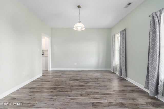 empty room with baseboards, visible vents, and wood finished floors