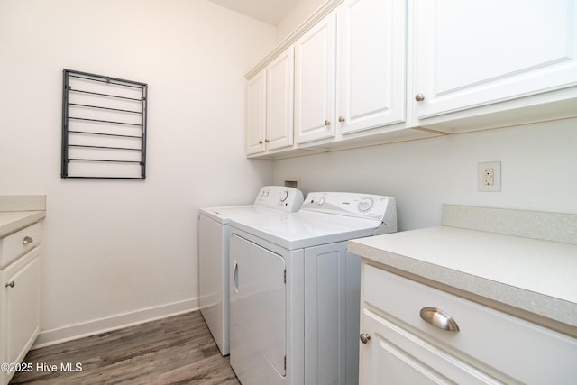 clothes washing area with washing machine and clothes dryer, baseboards, wood finished floors, and cabinet space