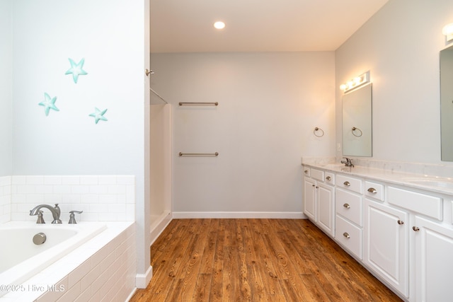 full bathroom featuring a sink, double vanity, baseboards, wood finished floors, and tiled tub