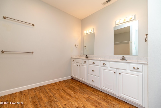 full bathroom featuring visible vents, double vanity, wood finished floors, baseboards, and a sink
