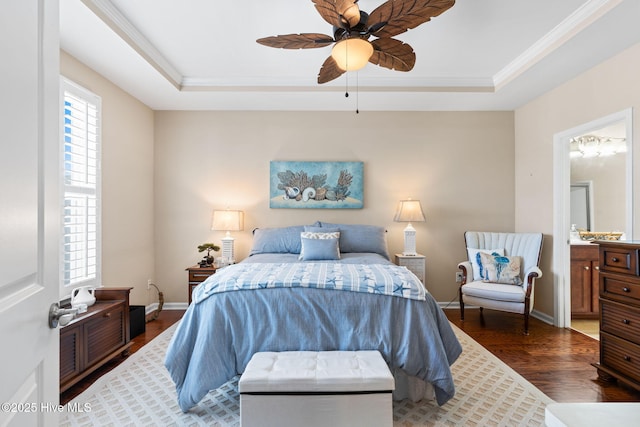 bedroom featuring a tray ceiling, wood finished floors, ornamental molding, baseboards, and ensuite bath