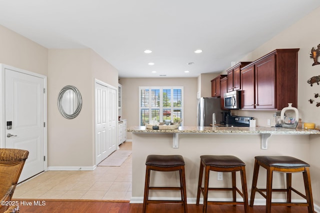 kitchen featuring stainless steel appliances, a peninsula, light stone countertops, a breakfast bar area, and recessed lighting