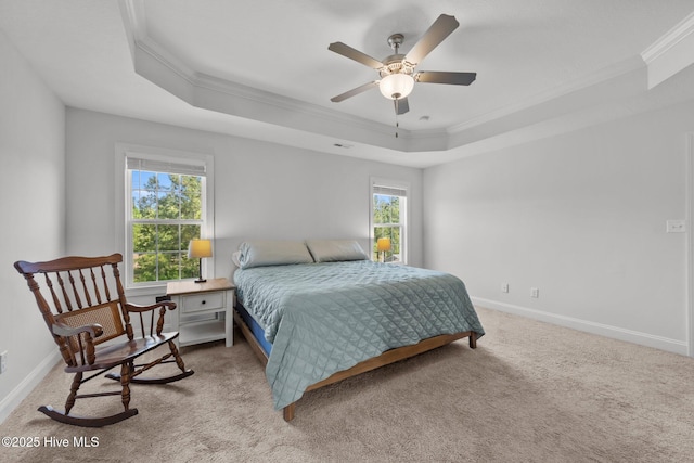carpeted bedroom with a tray ceiling, crown molding, baseboards, and ceiling fan