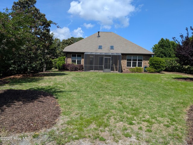 back of property with a lawn, a sunroom, and roof with shingles