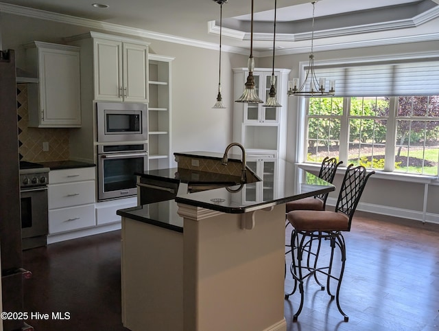 kitchen with dark countertops, appliances with stainless steel finishes, a sink, a center island with sink, and ornamental molding