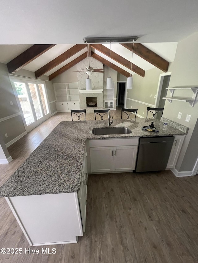 kitchen with stainless steel dishwasher, a fireplace, a sink, open floor plan, and vaulted ceiling with beams