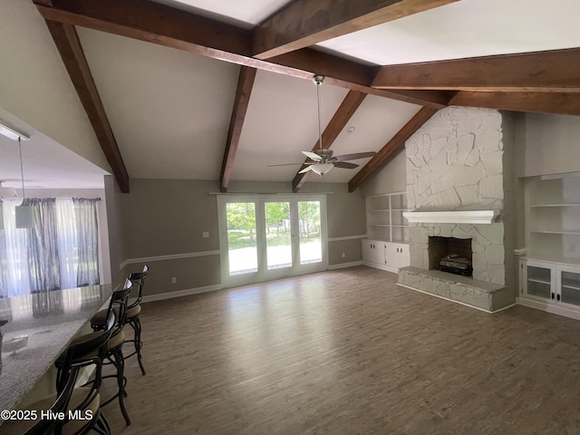 living area featuring built in features, wood finished floors, baseboards, a stone fireplace, and ceiling fan