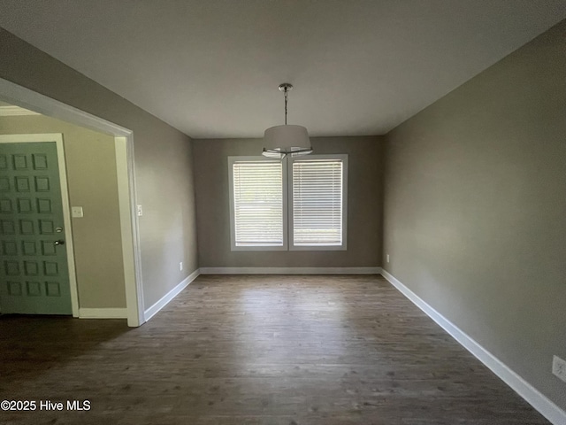 unfurnished dining area with dark wood-style flooring and baseboards