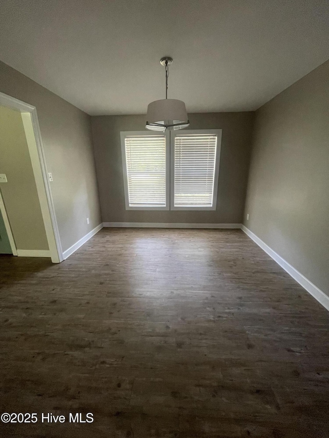 unfurnished dining area with baseboards and dark wood-style flooring