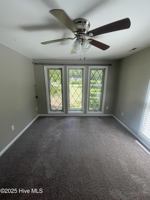 carpeted empty room featuring a ceiling fan, baseboards, visible vents, and plenty of natural light