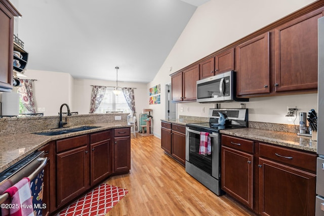 kitchen featuring appliances with stainless steel finishes, a sink, light wood finished floors, stone counters, and vaulted ceiling