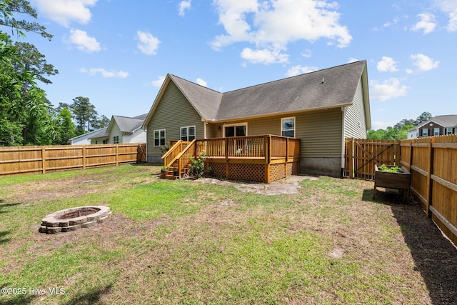 rear view of house featuring a fenced backyard, a wooden deck, a lawn, and a fire pit