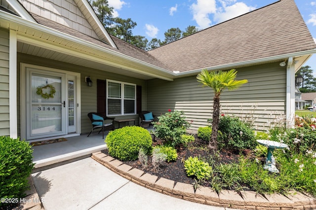 entrance to property with covered porch and a shingled roof